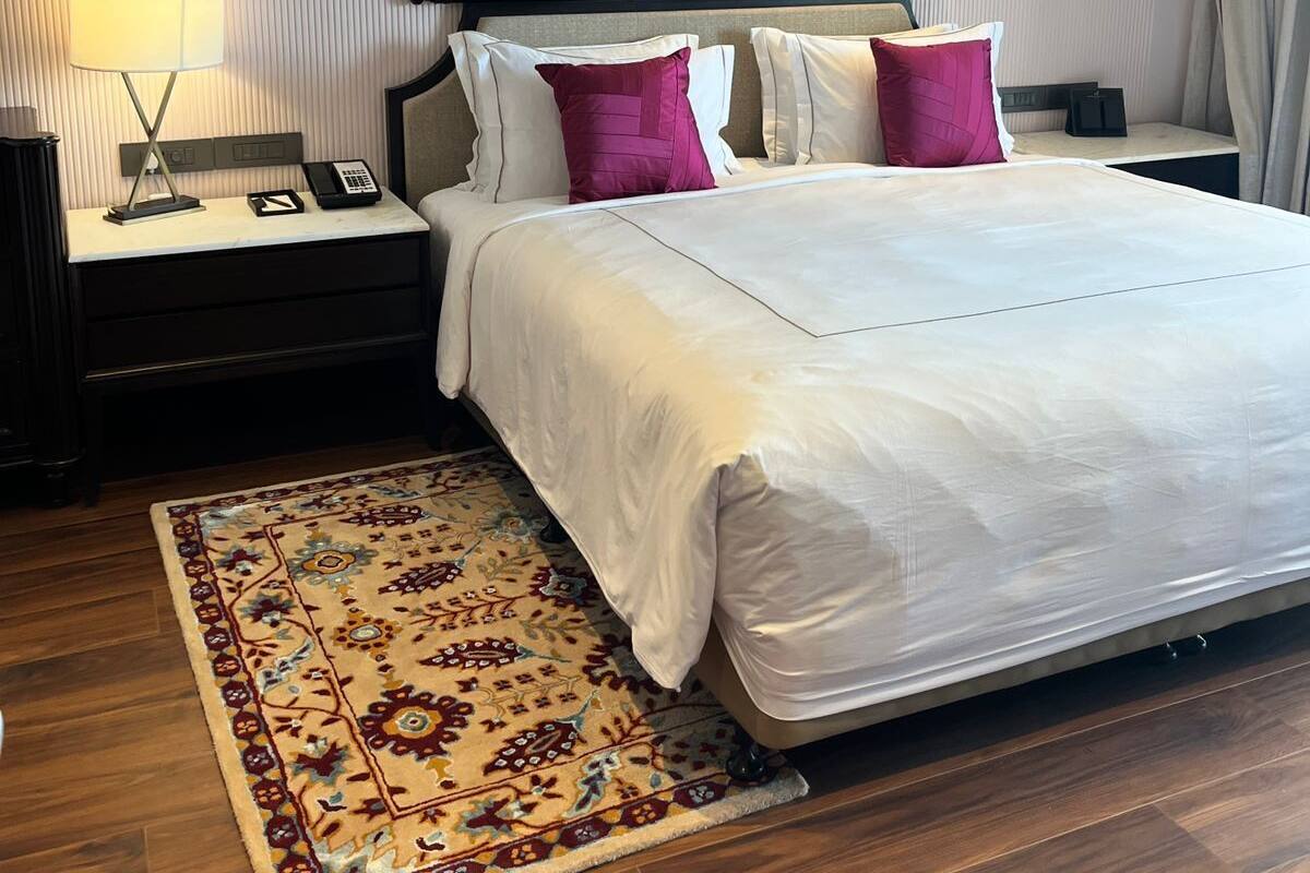 A hotel room with a large bed, a nightstand with a lamp, a phone, and a decorative rug.