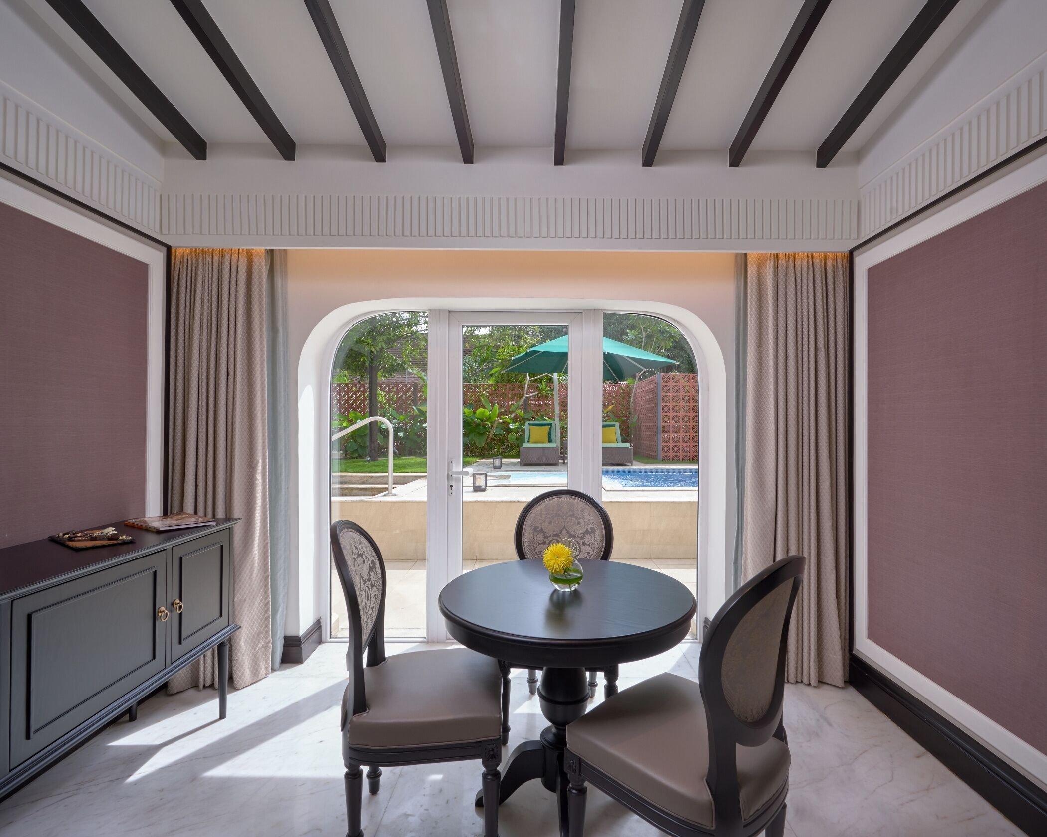 A room with a dining table, chairs, a cabinet, and a view of a pool and outdoor area.