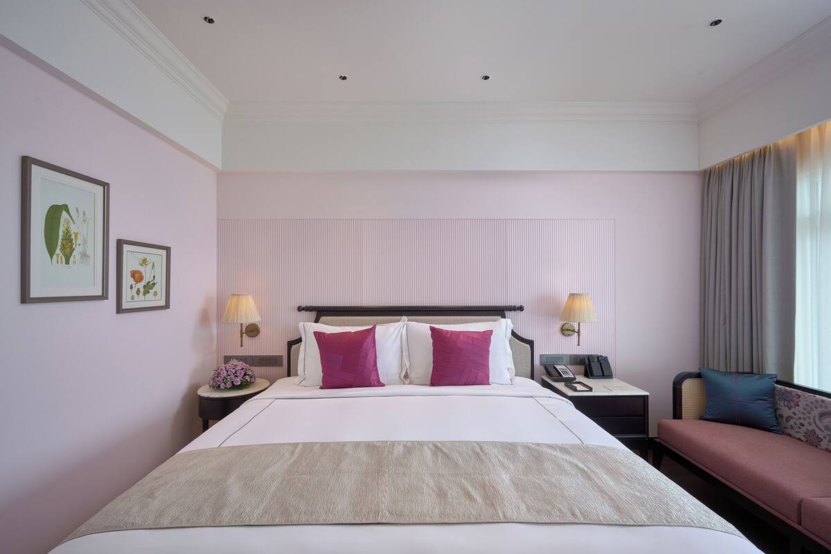 A hotel room with a large bed, bedside tables, a nightstand, a sofa, and a window with curtains.