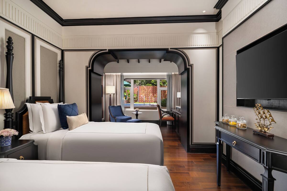 A hotel room with two beds, a desk, a TV, and a view of the outside.