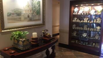 A hallway with a framed painting of a building, a display case with jewelry, a table with decorative items, and a wall-mounted telephone.