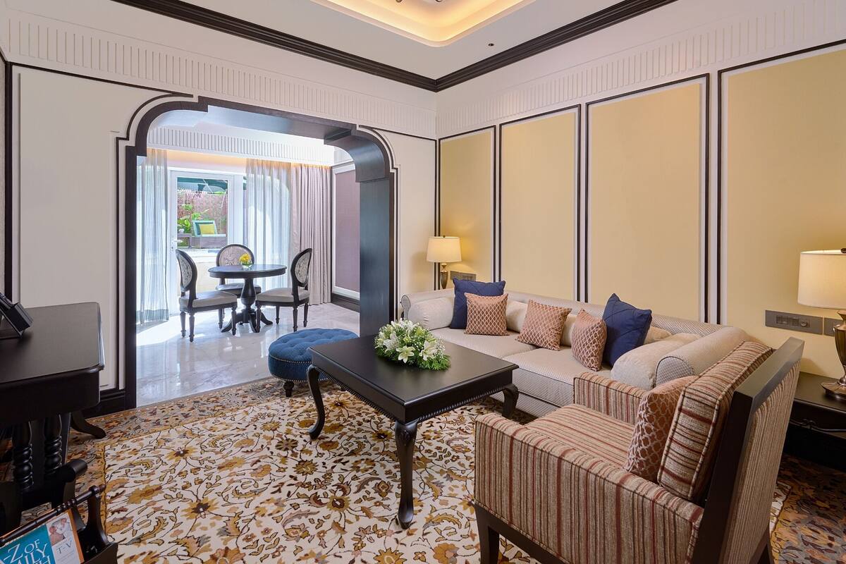 A hotel room with a sofa, armchair, dining table, and a chandelier.