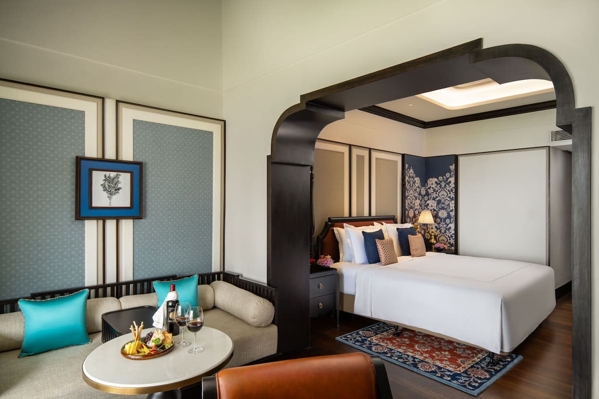 A hotel room with a bed, a seating area with a table, and a decorative wall.