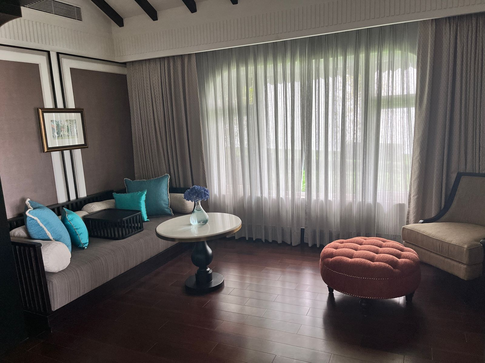 A living room with a sofa, ottoman, and a table with a vase.