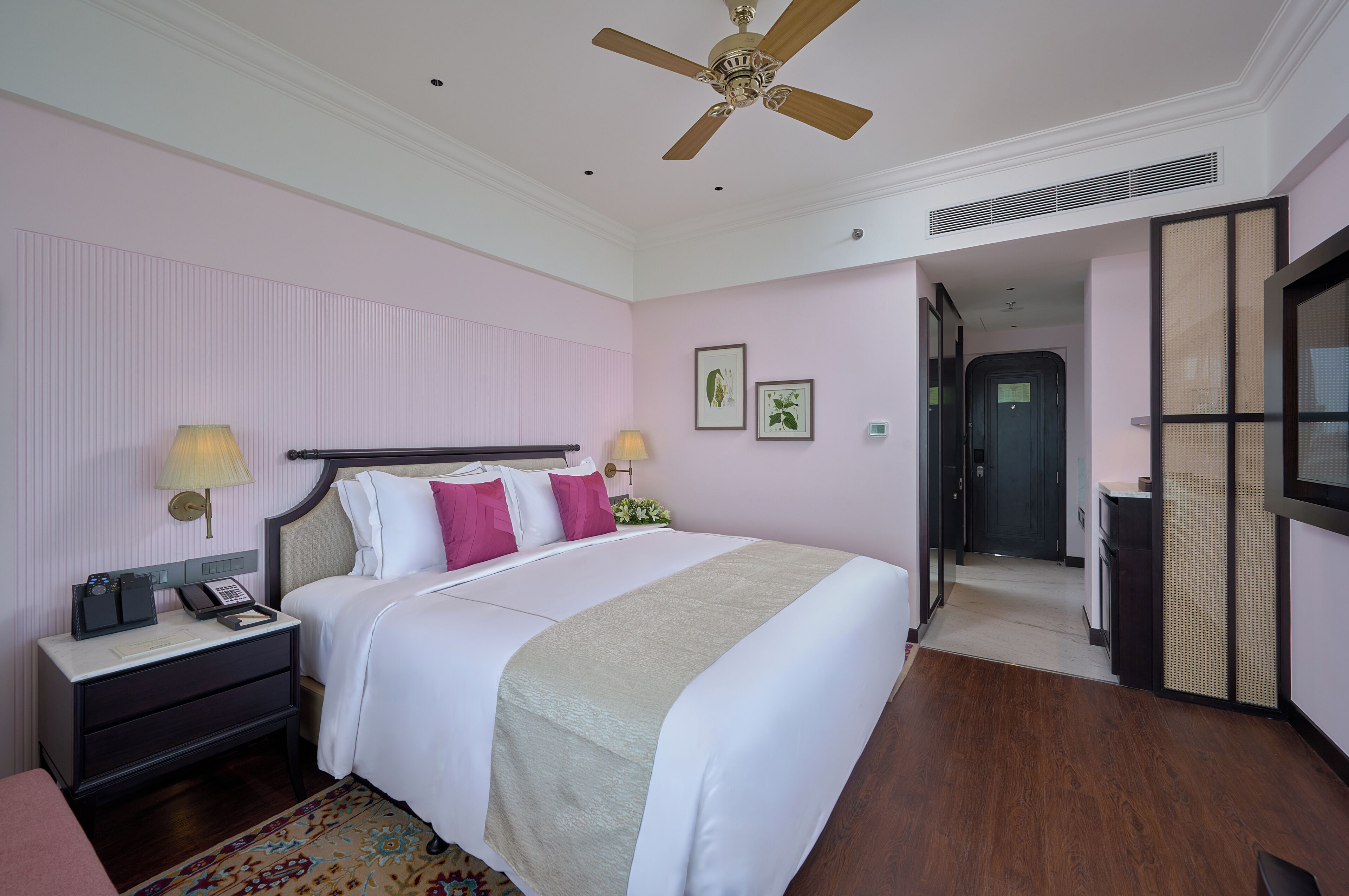 Una habitación de hotel con una cama, mesitas de noche, un ventilador de techo, un escritorio y una puerta que da a otra habitación.