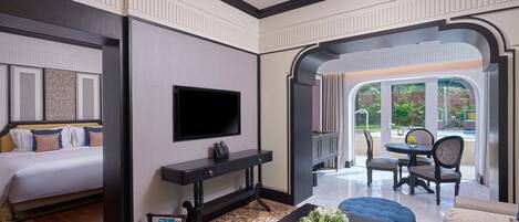 Habitación de hotel con cama, televisor montado en la pared, una mesita con un arreglo floral y una zona de estar con sofá y sillones.