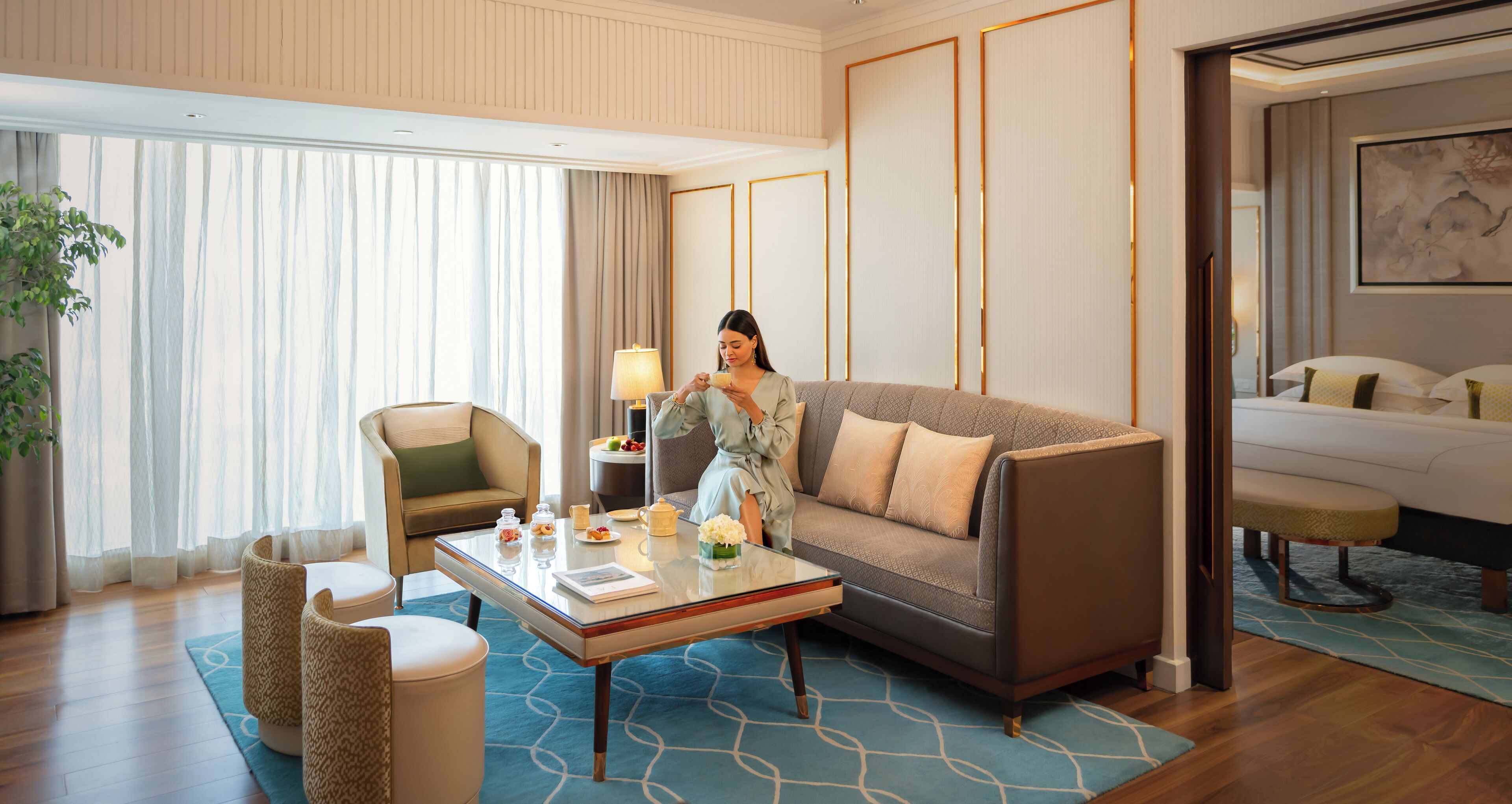 Habitación de hotel con sofá, sillón, mesa de centro y una mesa de comedor con lámpara.
