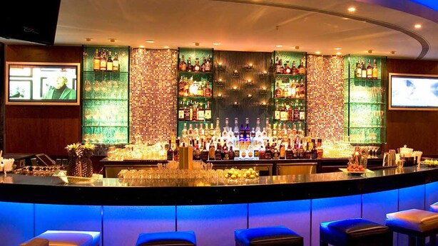 Una zona de bar con mostrador, varias estanterías llenas de botellas y una pantalla de televisión.