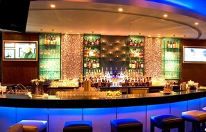 A bar area with a counter, multiple shelves of bottles, and a television screen.