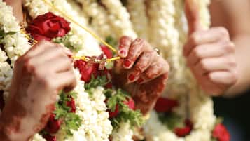 Hænder pyntet med henna holder en guirlande af hvide og røde blomster.