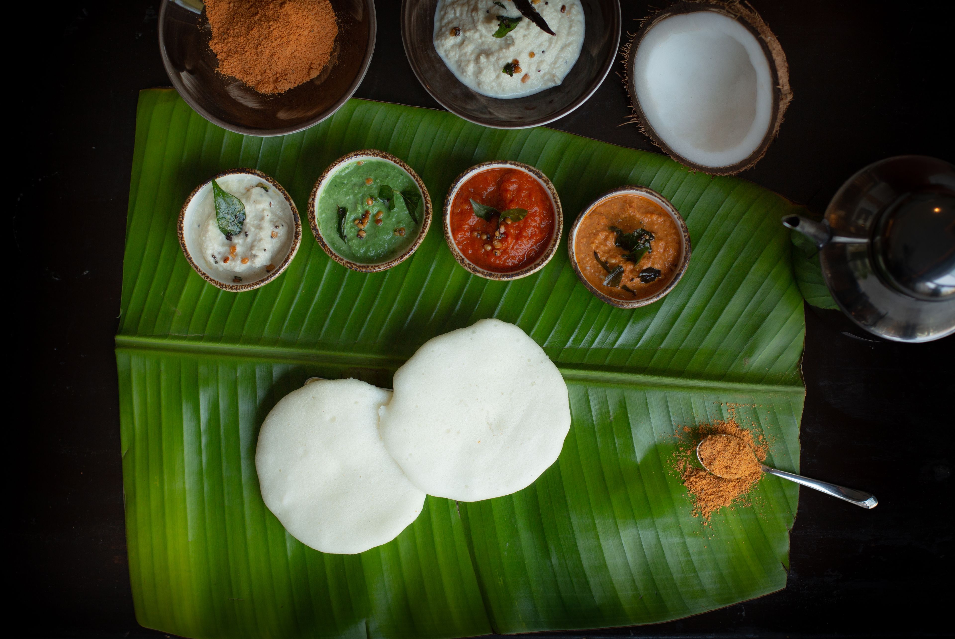 Comida tradicional del sur de la India con idlis y chutneys sobre una hoja de plátano.