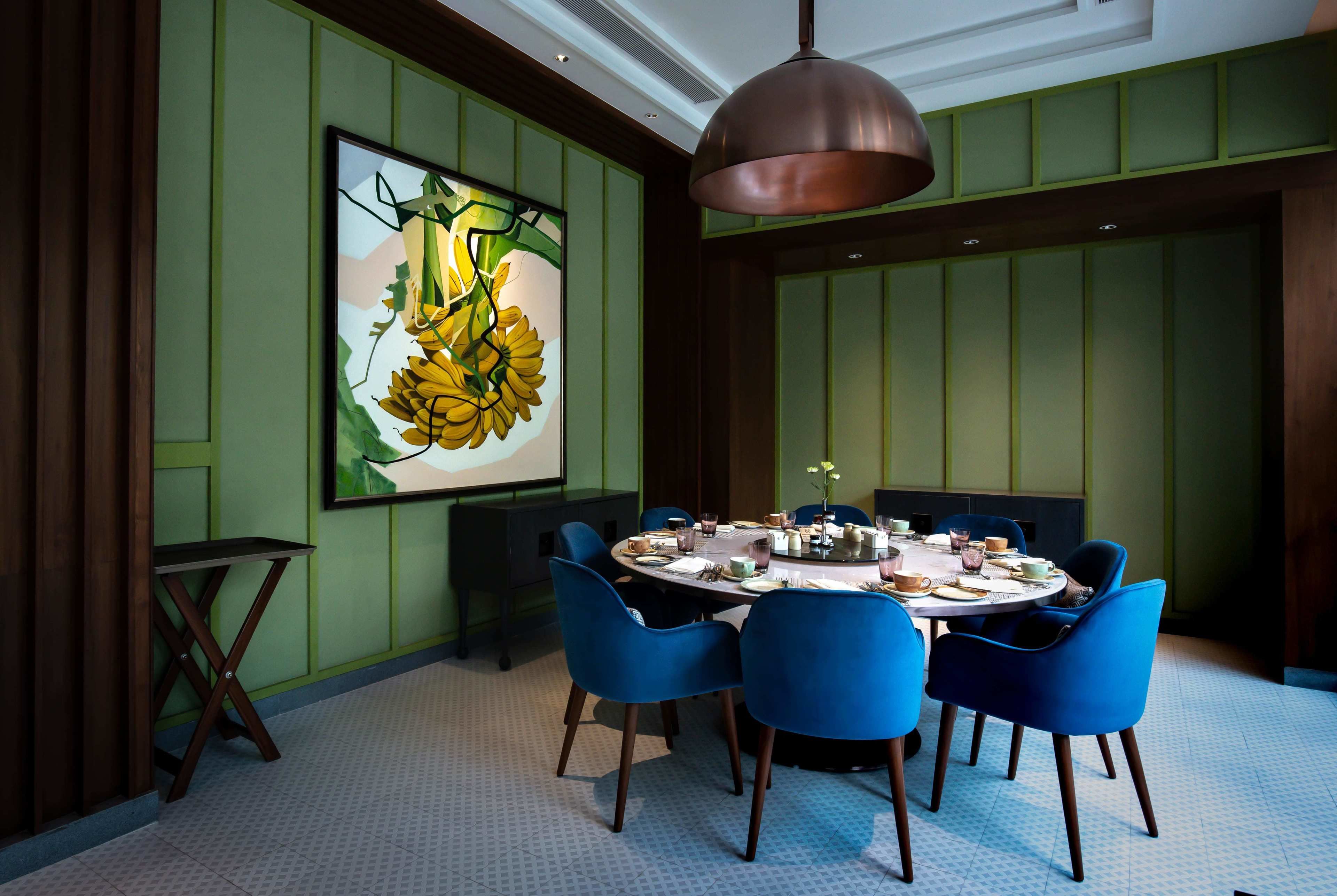 Comedor con una mesa redonda, sillas azules y un cuadro grande de girasoles en la pared.