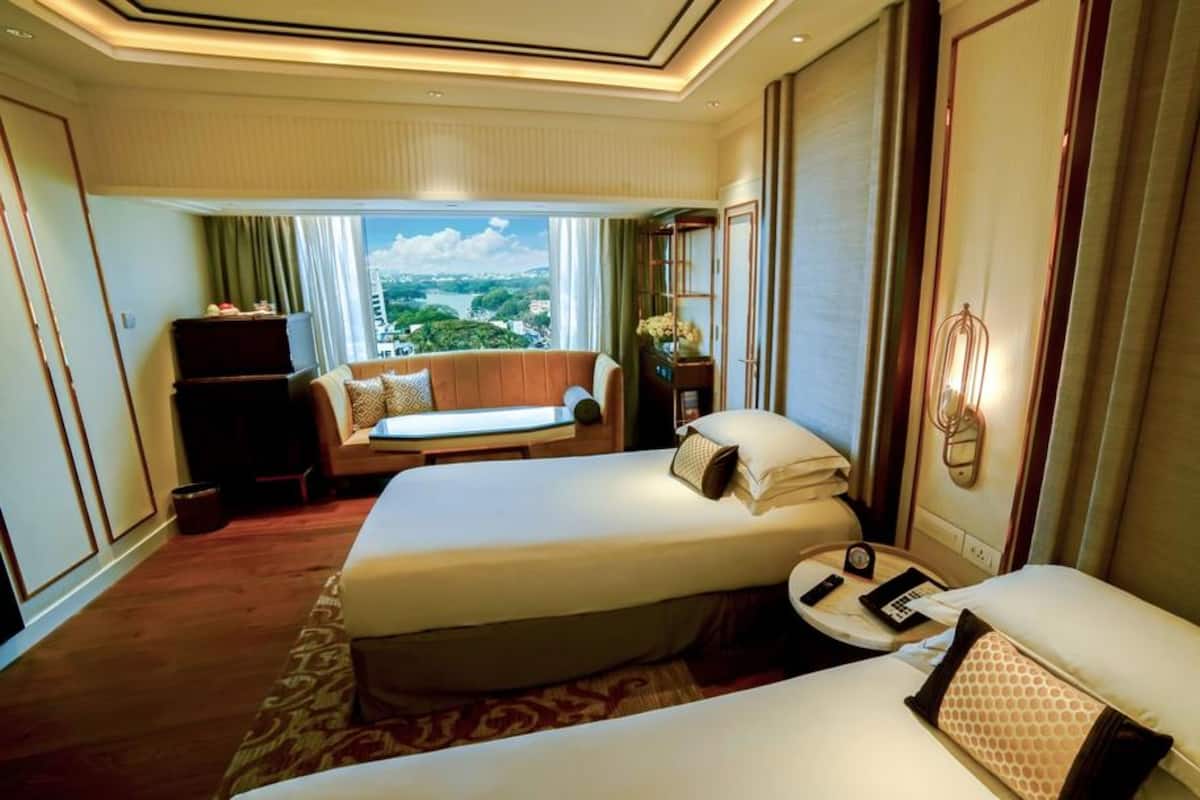 A hotel room with two beds, a sofa, a desk, and a view of a cityscape.