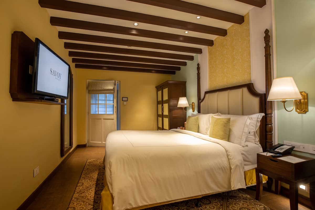 A hotel room with a large bed, a television, a desk with a lamp, and a wooden headboard.