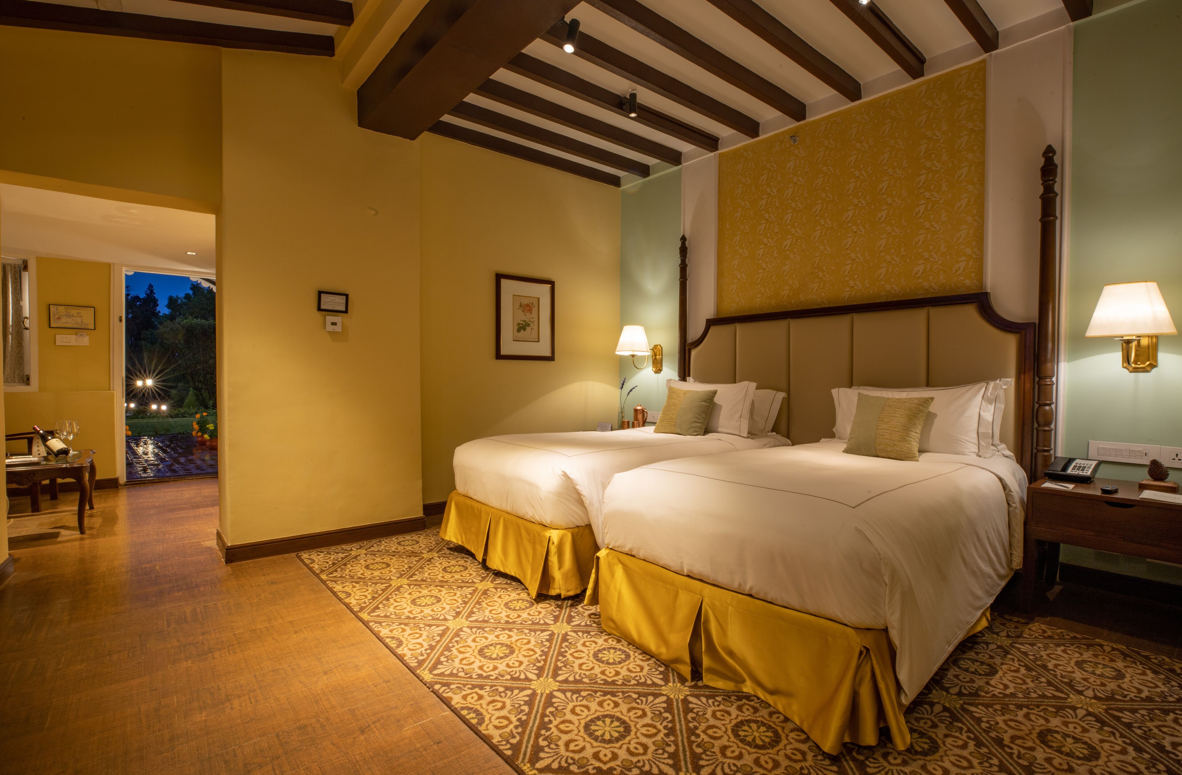 A hotel room with two beds, a wooden ceiling, patterned carpet, and a night view outside.