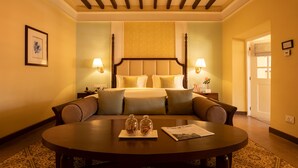 Habitación de hotel con cama con dosel, dos lámparas de noche, una mesa redonda con una bandeja de aperitivos y un cuadro en la pared.