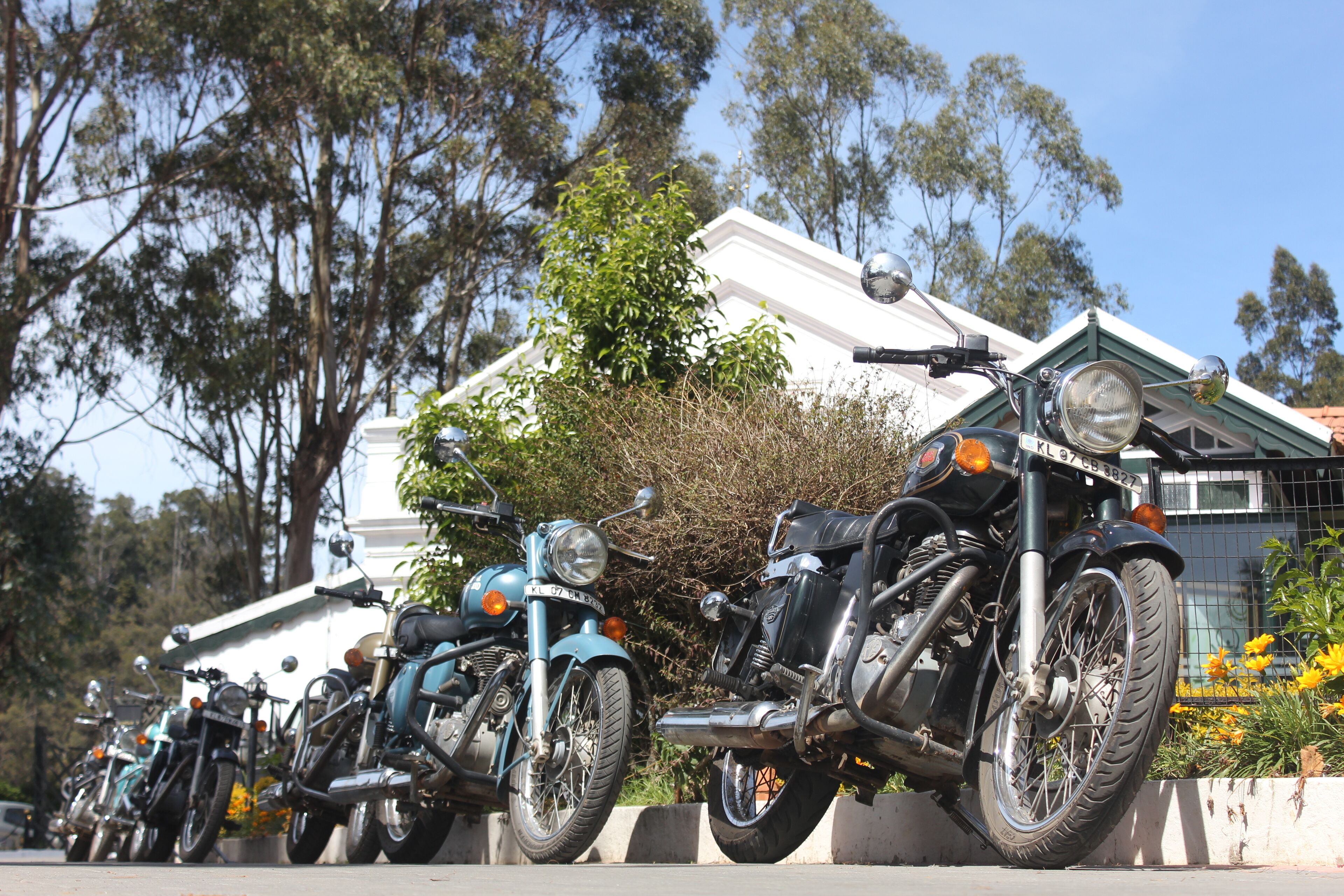 A row of motorcycles parked in front of a building with a white facade and green roof.
