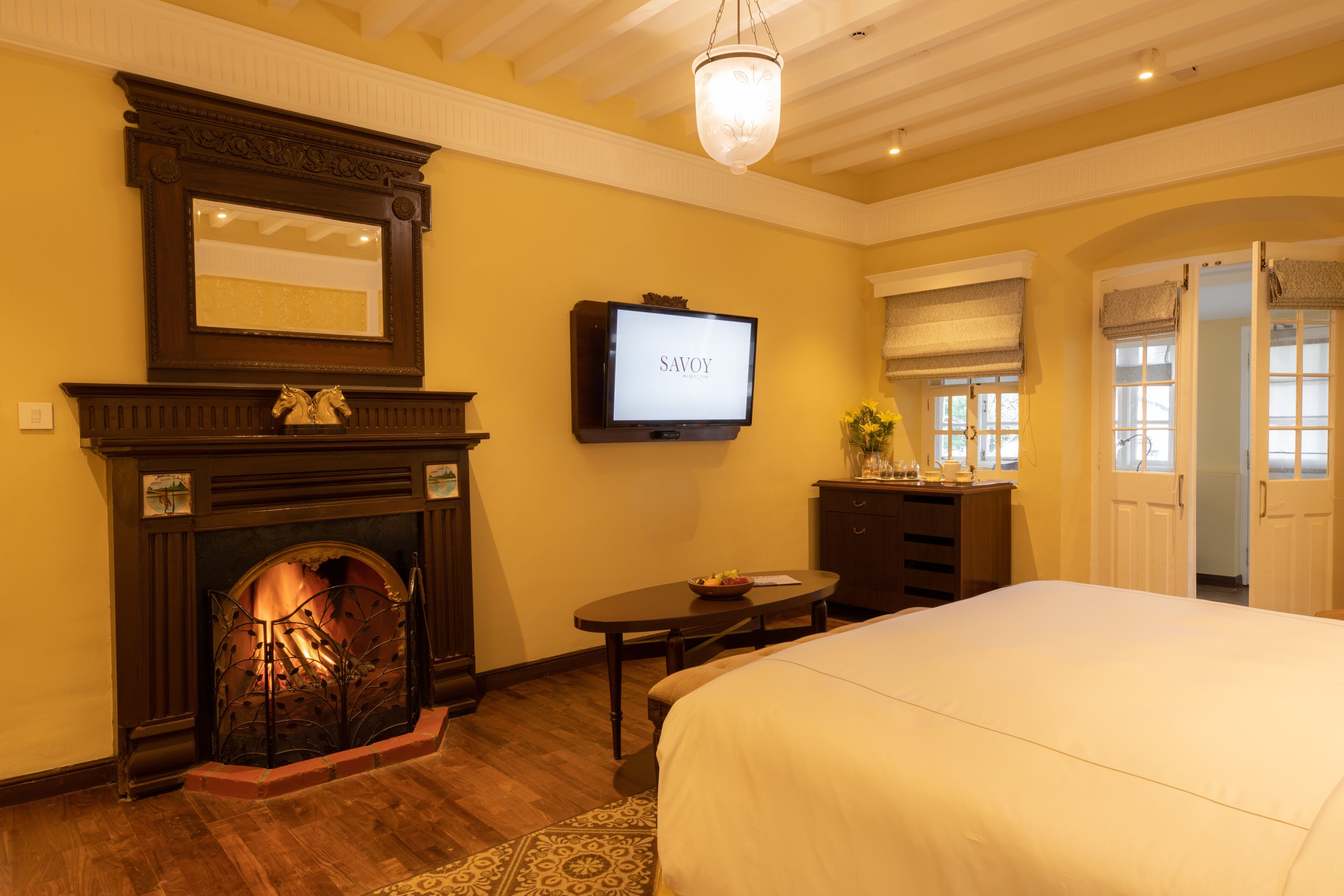 A hotel room with a fireplace, a television, a bed, a desk, and a door leading to another room.