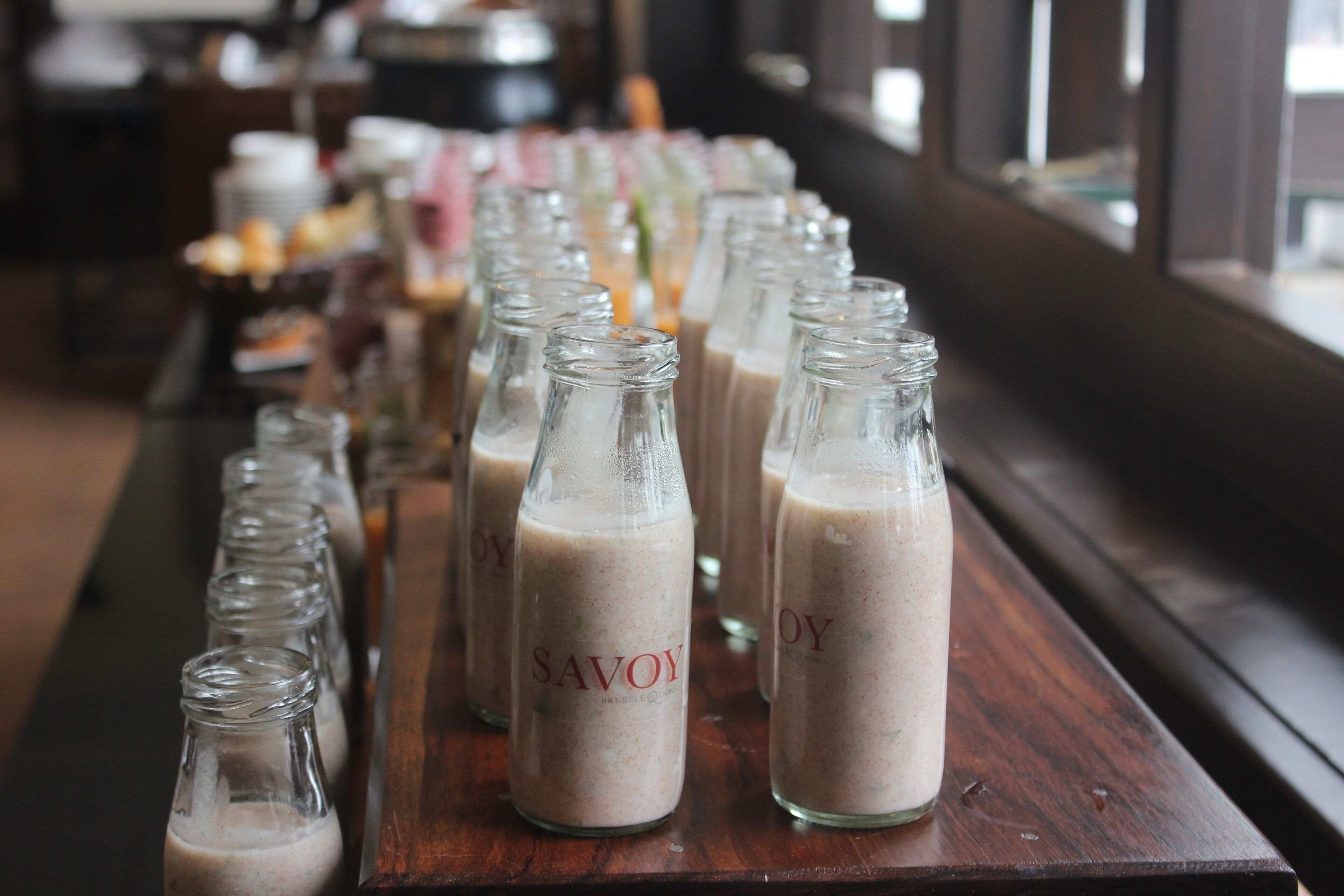 A row of glass bottles labeled "SAVOY" on a wooden table in a room with large windows.