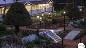 Propiedad residencial bien iluminada con jardín, un pequeño puente y un camino que lleva a la entrada.