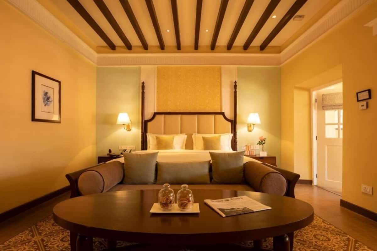 A hotel room with a bed, two bedside lamps, a round table with a magazine, and a framed picture on the wall.