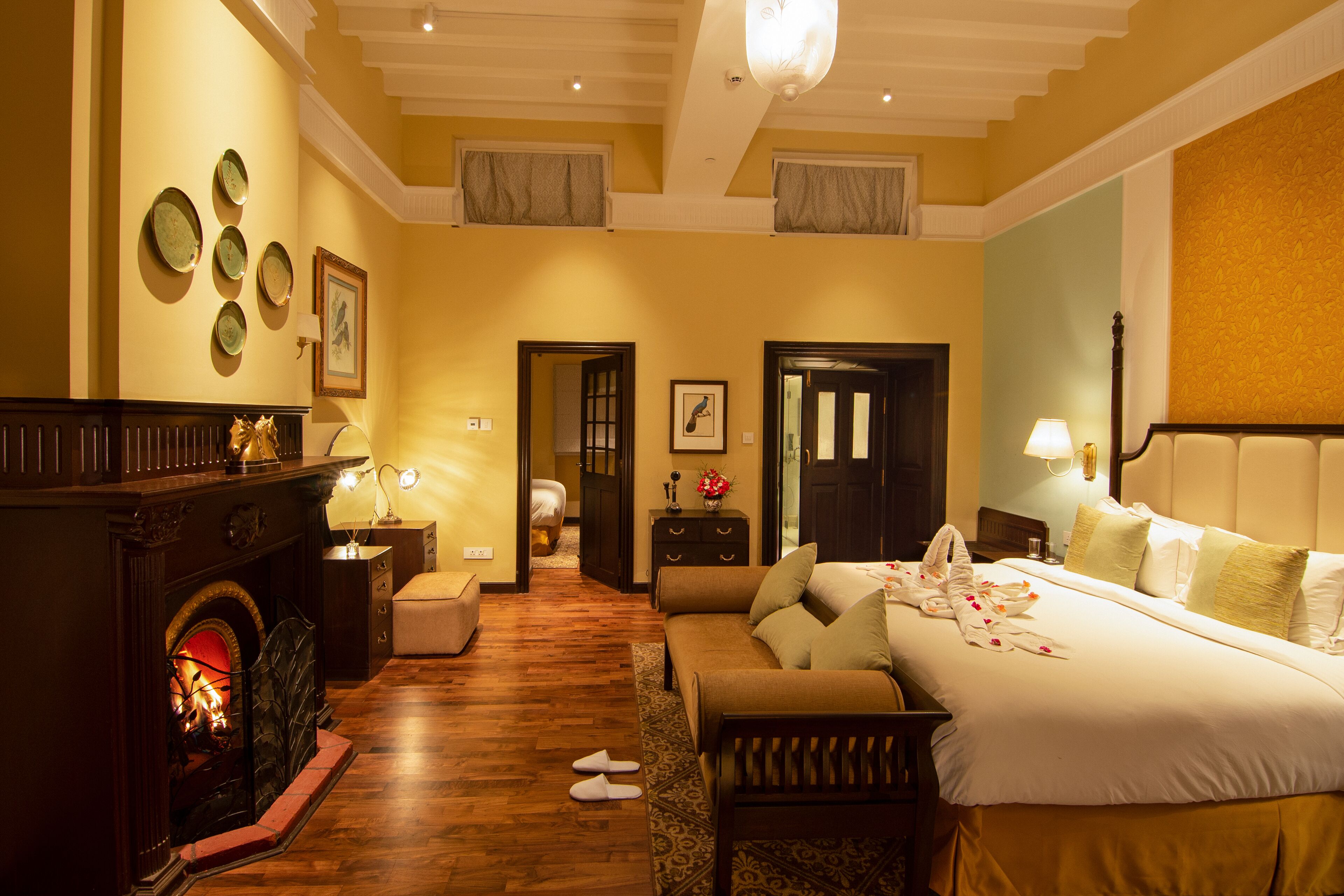 A hotel room with a fireplace, a sofa, a bed with pillows, and a nightstand with a lamp.