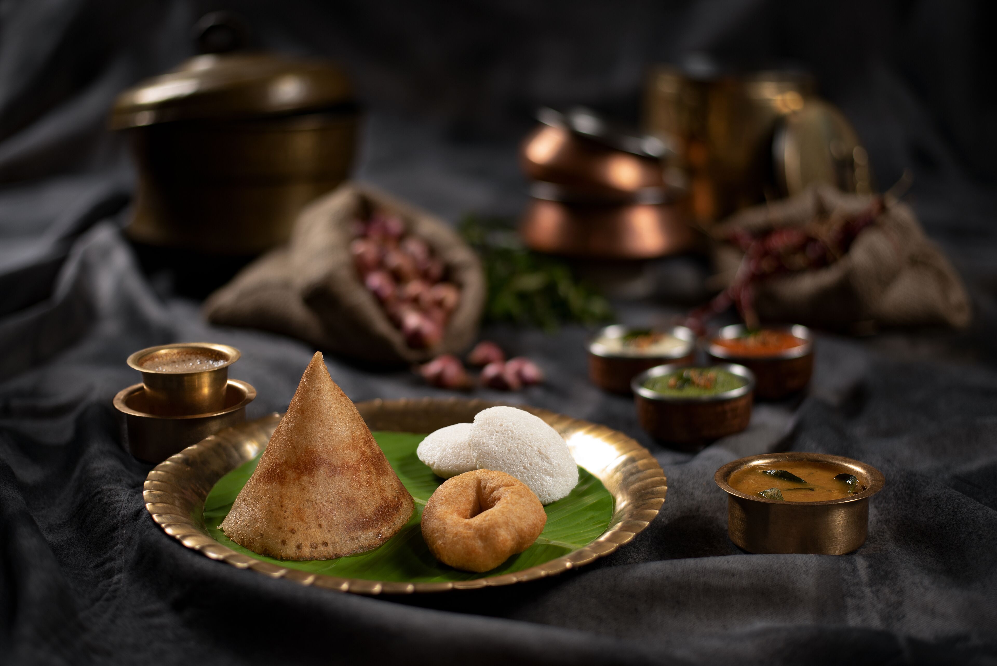 A traditional South Indian meal with dosas and sambar on a banana leaf, accompanied by brass utensils.