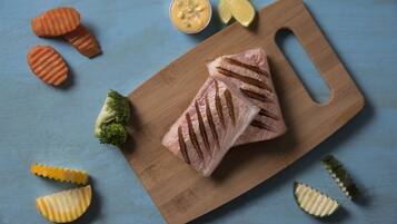 Una tabla de madera con un trozo de carne y diferentes verduras sobre una superficie azul.