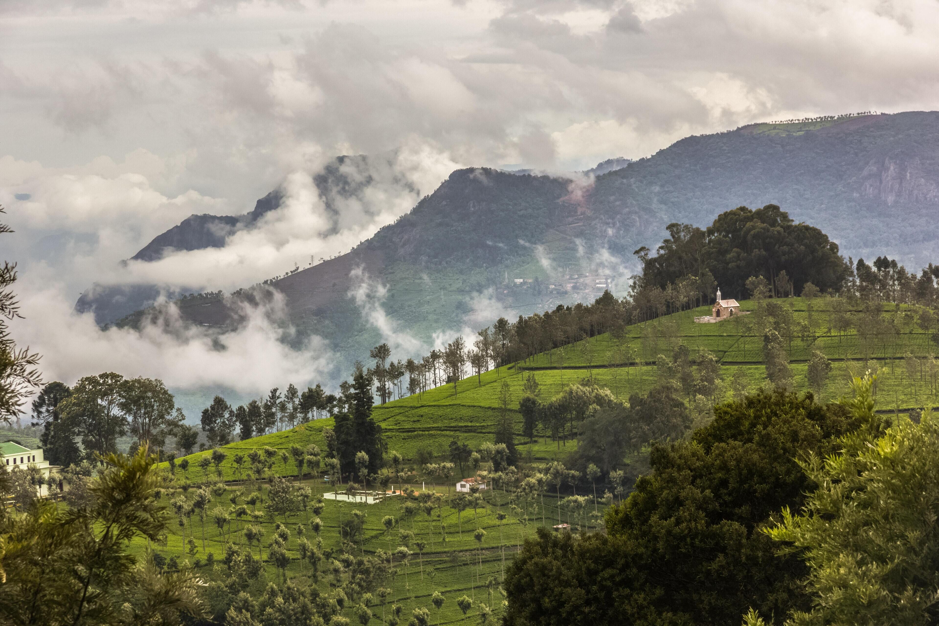 A lush green landscape with terraced fields, a small white building, and a hill with a church.