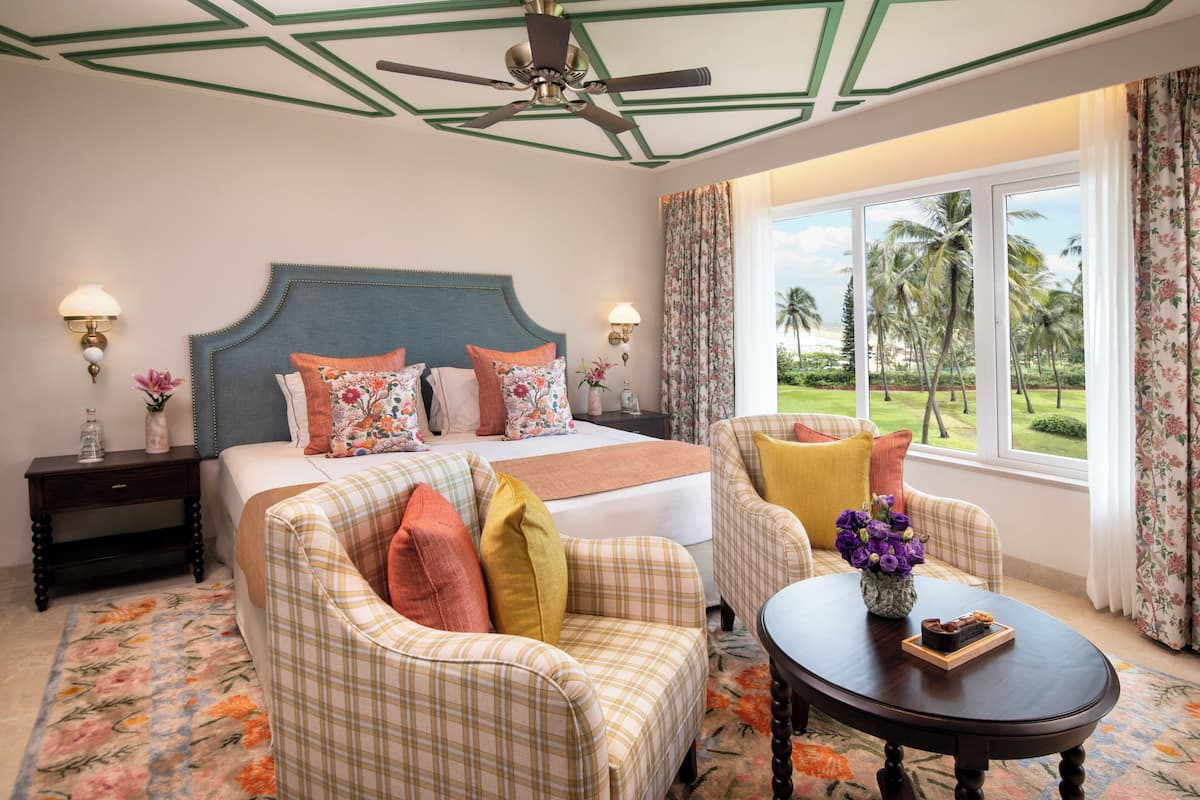 A hotel room with a bed, two armchairs, a coffee table, and a view of palm trees.