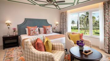 A hotel room with a bed, two armchairs, a coffee table, and a view of palm trees.
