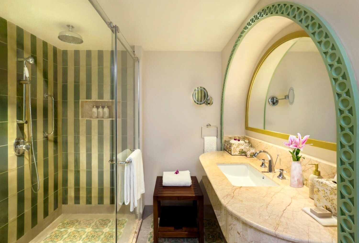 Un baño con cabina de ducha de vidrio, tocador con encimera de mármol, un espejo grande y un taburete pequeño.
