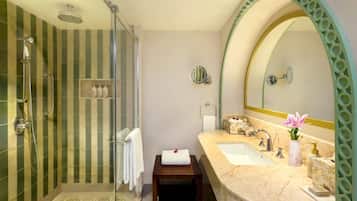 Un baño con cabina de ducha de vidrio, tocador con encimera de mármol, un espejo grande y un taburete pequeño.