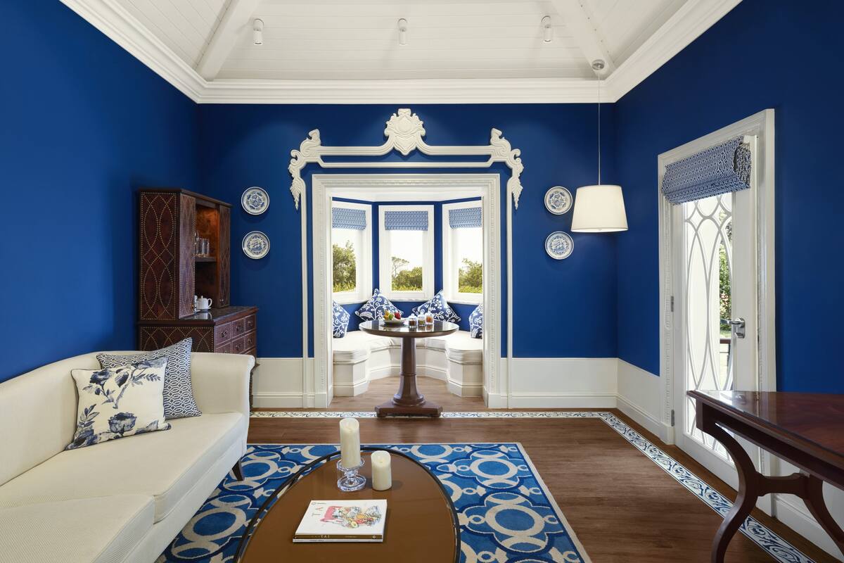 A room with blue walls, a white sofa, a wooden coffee table, and a decorative mirror.