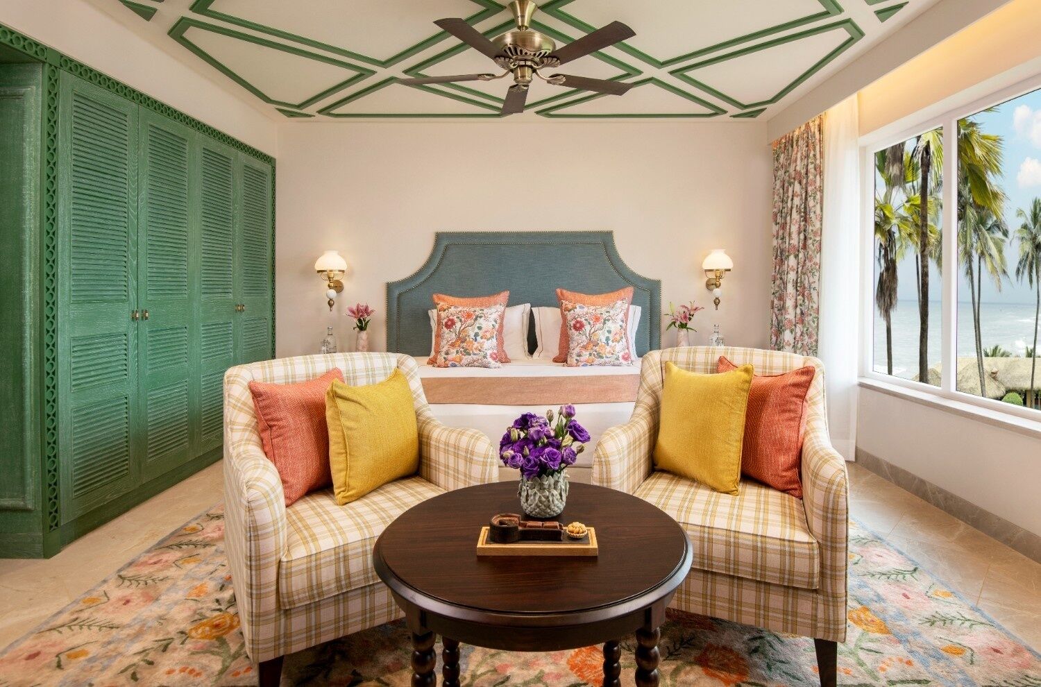 A hotel room with a bed, two sofas, a coffee table, and a view of palm trees through the window.
