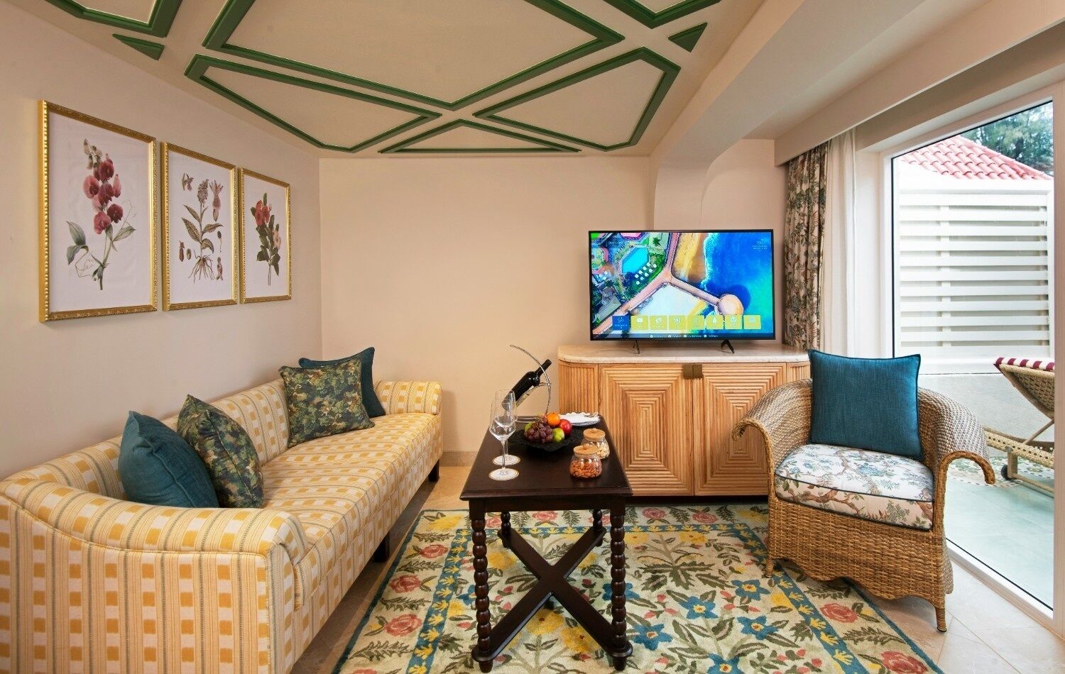 Una sala de estar con un sofá, una silla de mimbre, un televisor y una mesa con una botella y vasos.