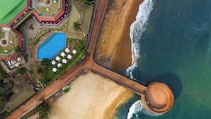 An aerial view of a beach resort with a swimming pool, beach umbrellas, and a circular pier structure. - Taj Fort Aguada Resort & Spa, Goa (Candolim)