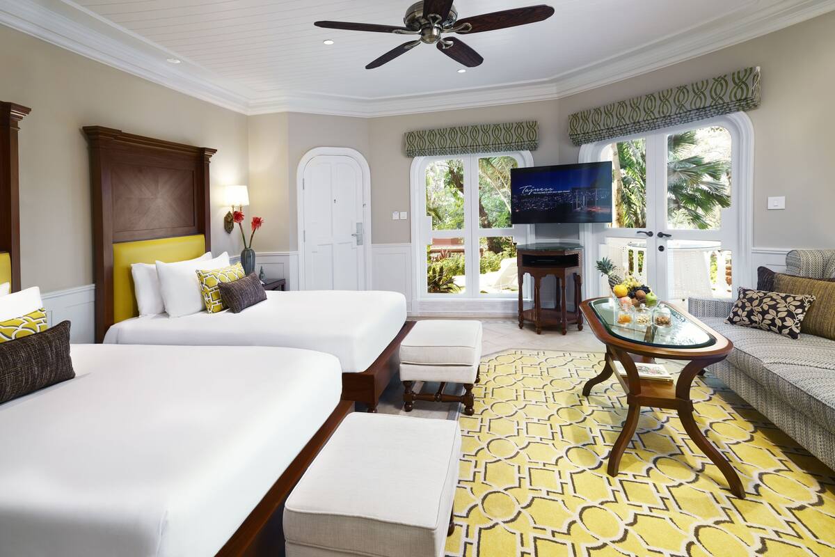A hotel room with two beds, a television, a glass coffee table, and a view of the outdoors.