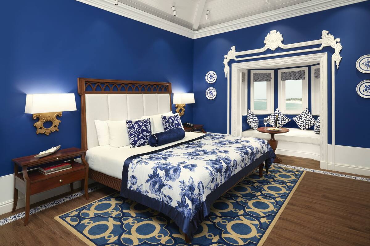 A bedroom with a large bed, a nightstand, a lamp, and a view of the sea through a window.