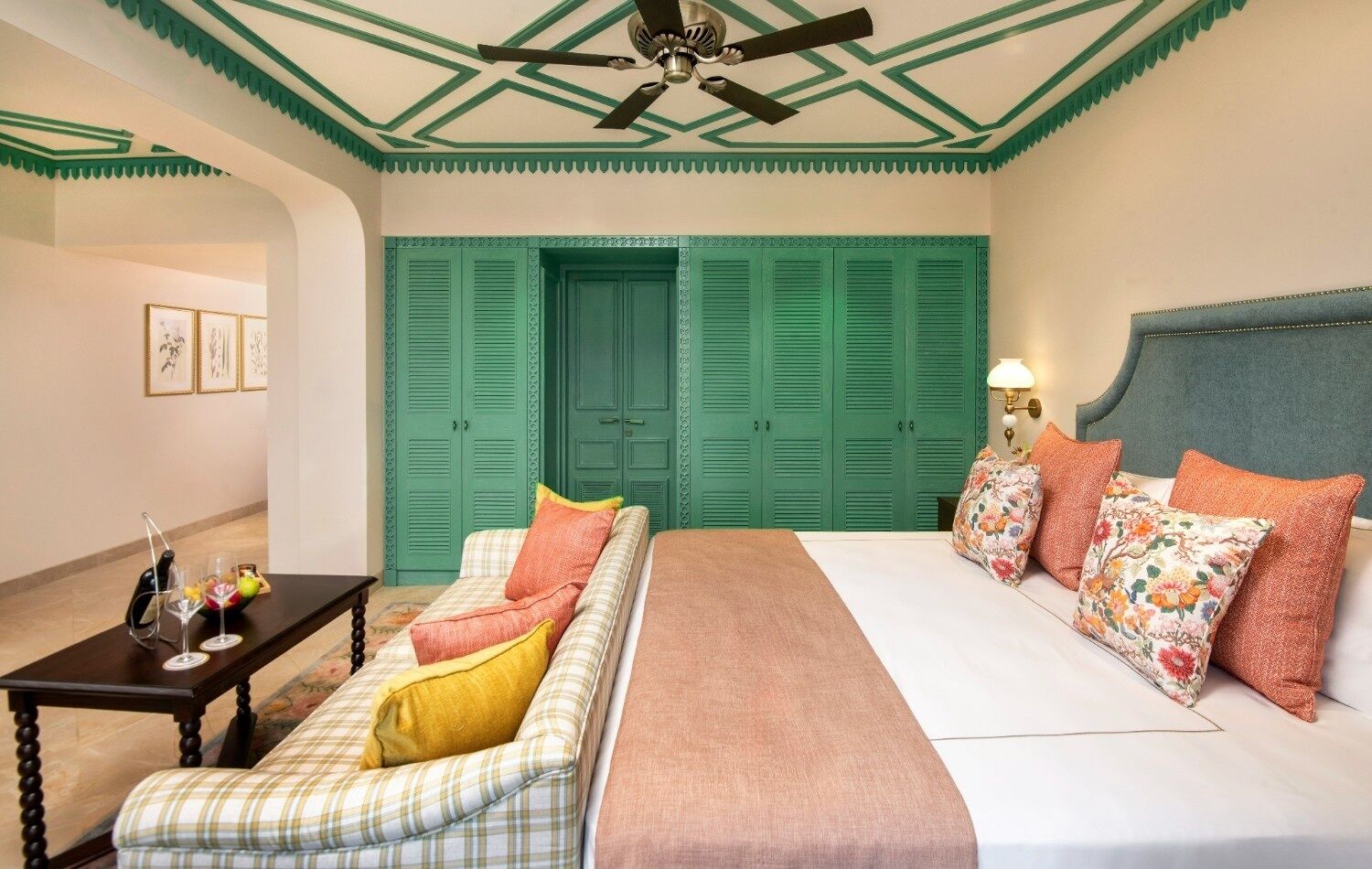 A hotel room with a bed, a sofa, a table with a lamp, and green doors.