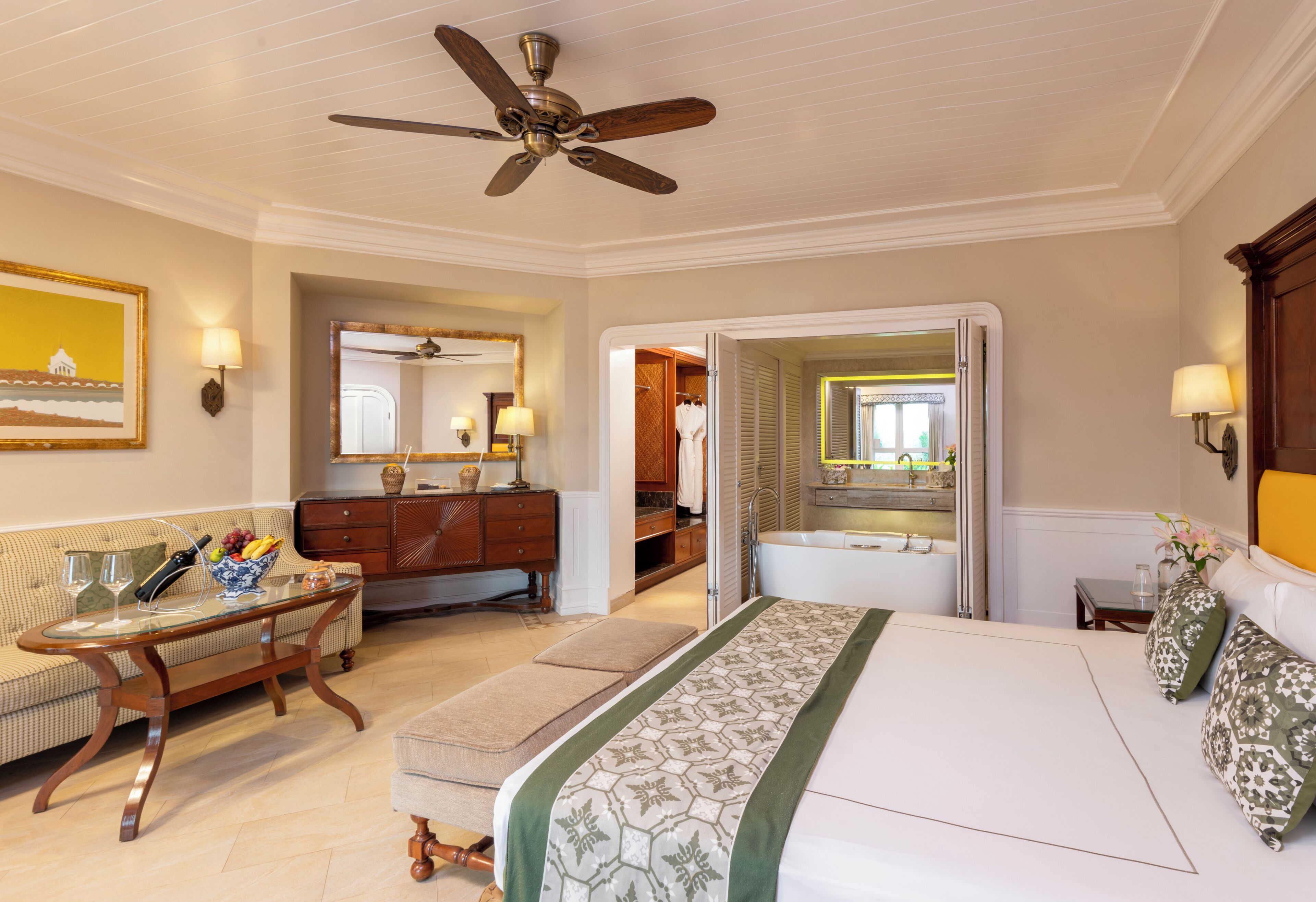 A hotel room with a bed, a sitting area with a table and chairs, a vanity with a mirror, and a ceiling fan.