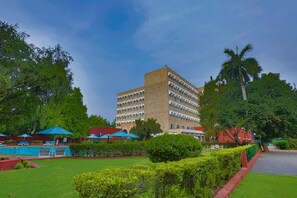 A hotel with a large building, a swimming pool, and green lawns.