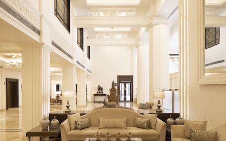 A spacious lobby with a high ceiling, a central seating area with a sofa and armchairs, and a decorative sculpture.