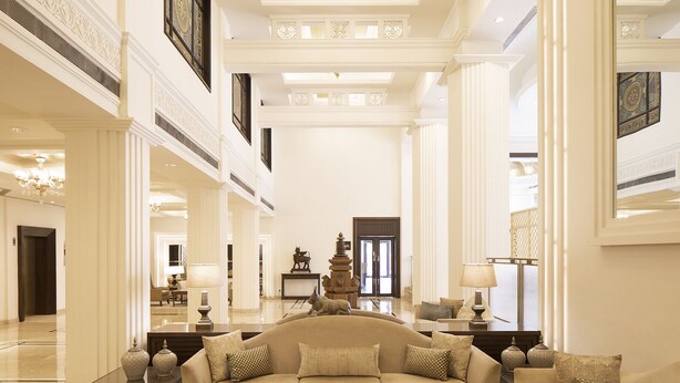 Un vestíbulo amplio con techo alto, un área de estar central con sofá y sillones, y una escultura decorativa.