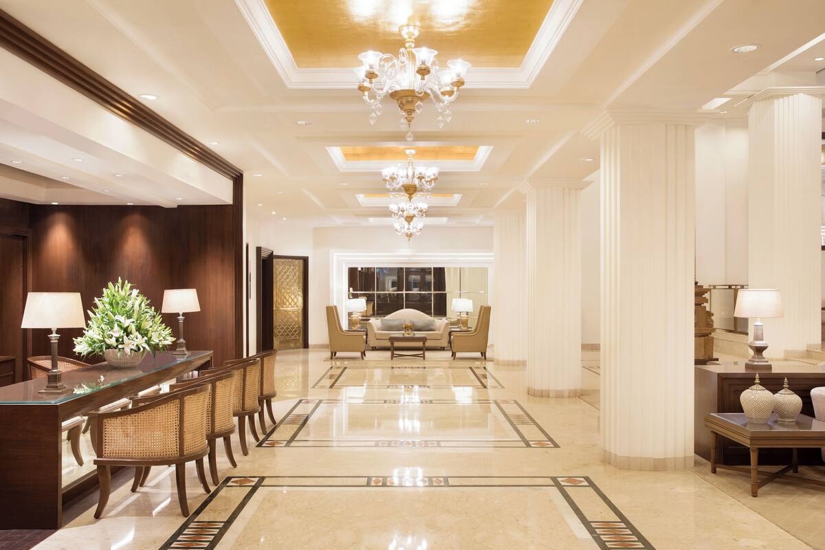 A spacious lobby with a long reception desk, comfortable seating, and a chandelier.