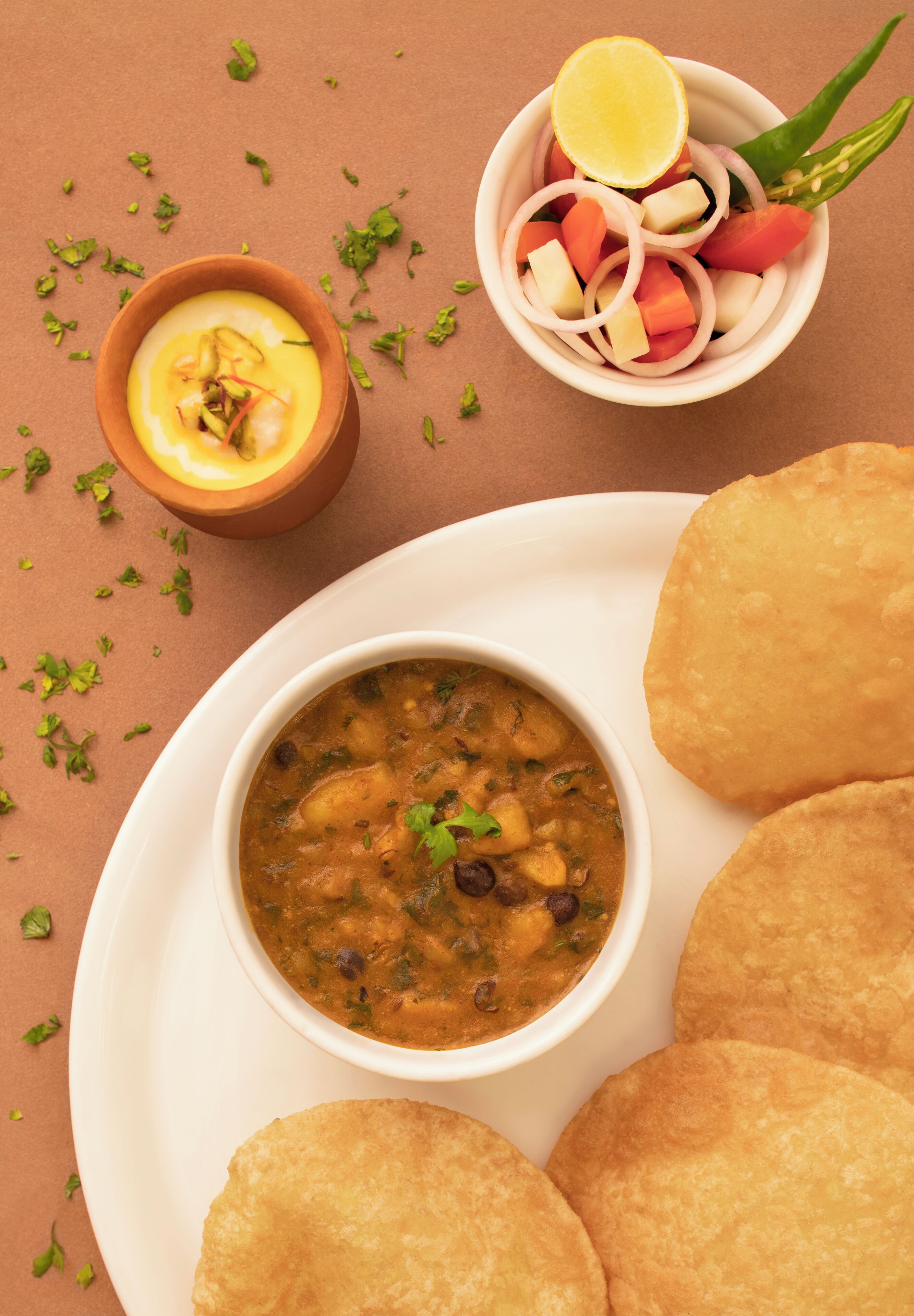 A plate with a bowl of soup, two pieces of flatbread, and a small bowl of sliced vegetables.