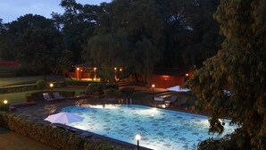 Una piscina con sillones de descanso y sombrillas, rodeada de setos y árboles cuidados.