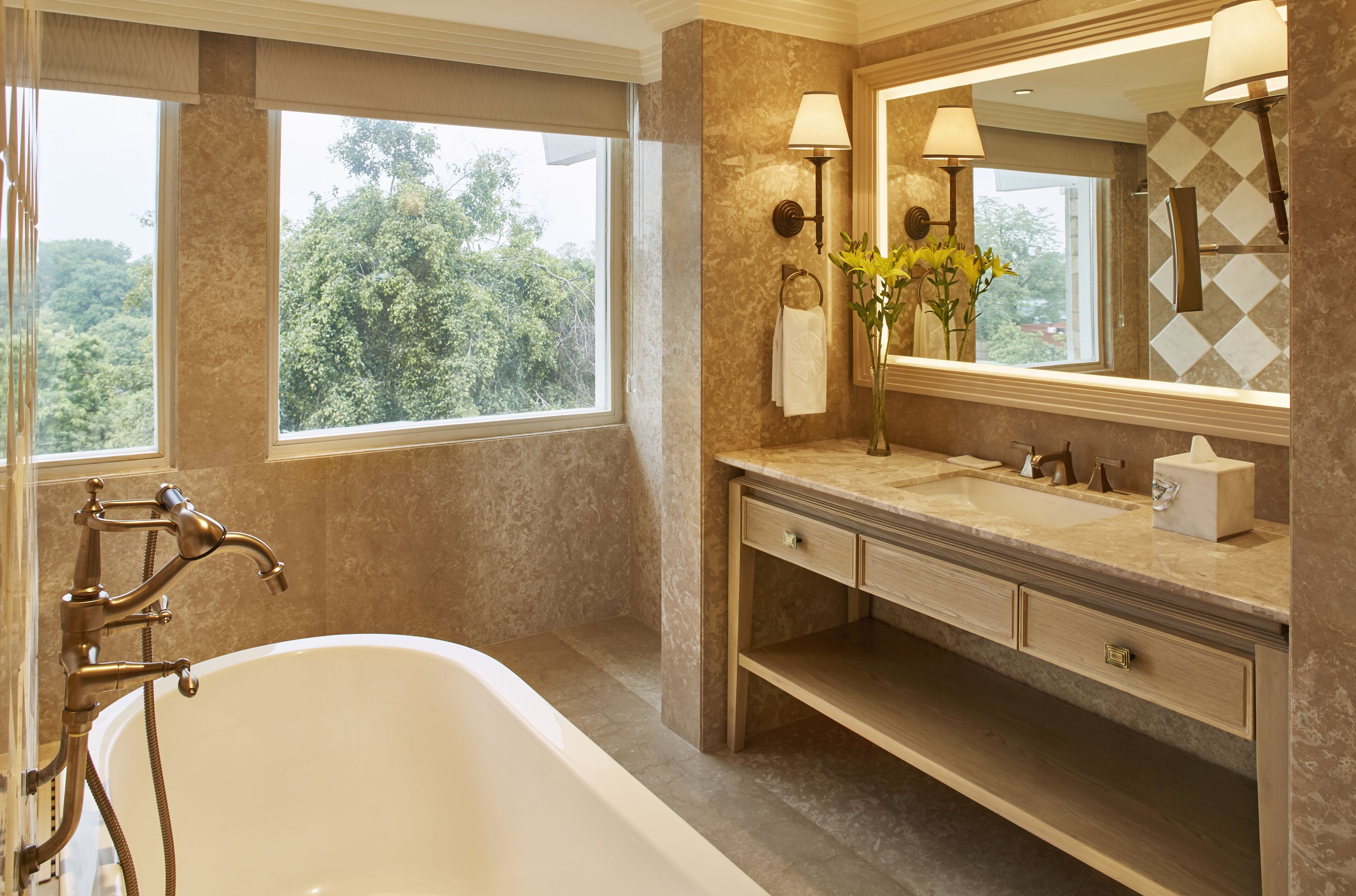 Un baño con bañera, tocador con espejo y ventana con vistas a árboles.