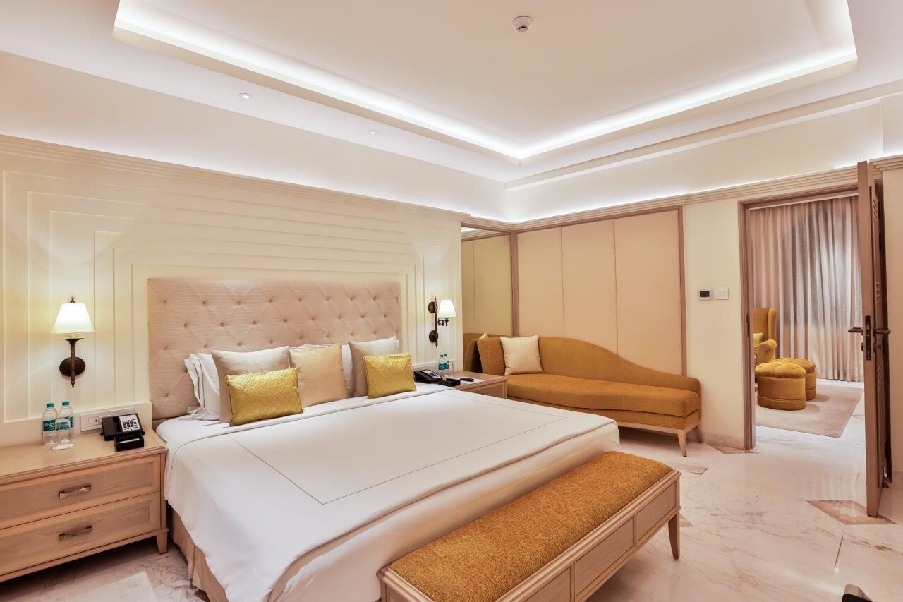 A modern hotel room with a large bed, a sofa, and a bench.