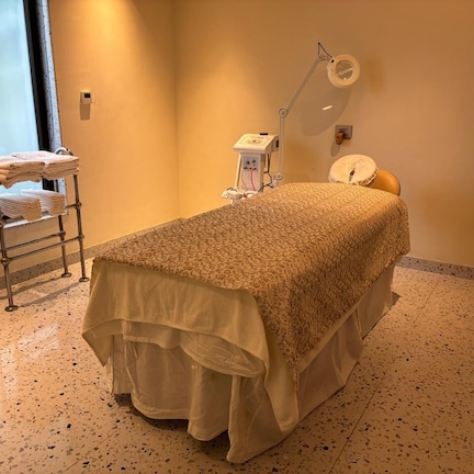 A room with a bed, a small table with towels, a wall-mounted lamp, and a window.